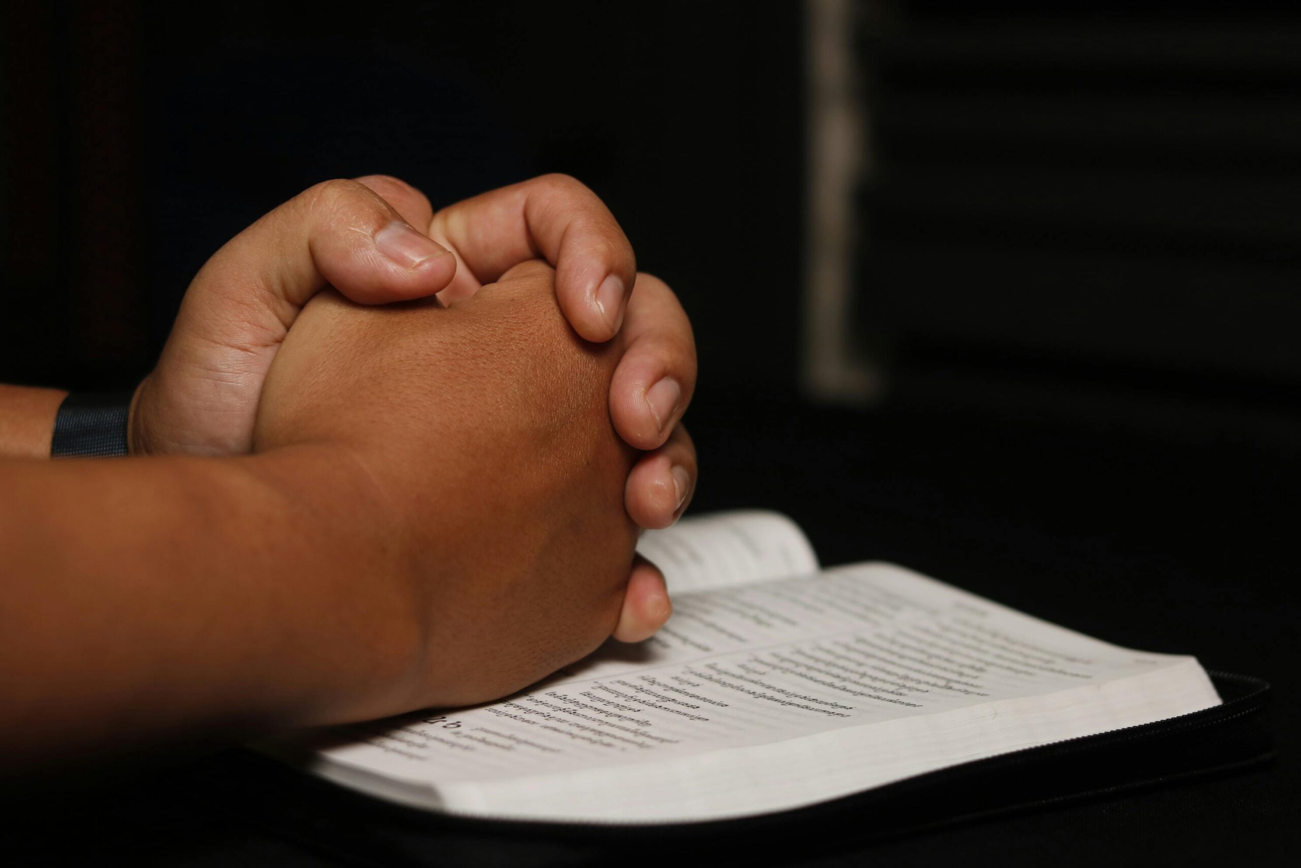 Hands clasped in prayer over an open book, symbolizing spirituality.