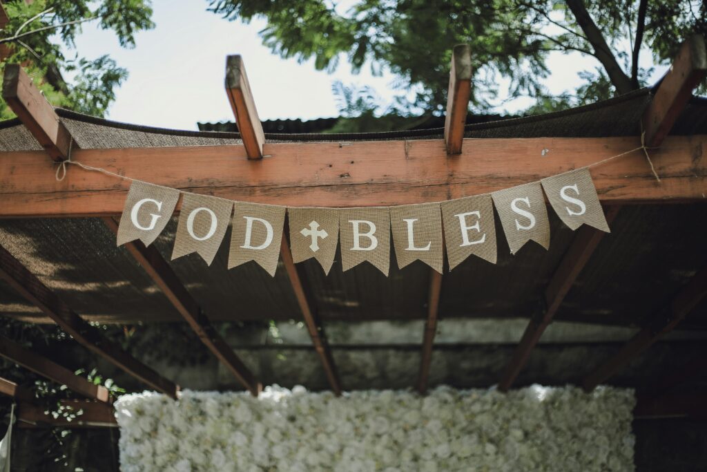 A charming pergola adorned with a 'God Bless' banner, set in a lush, outdoor environment.