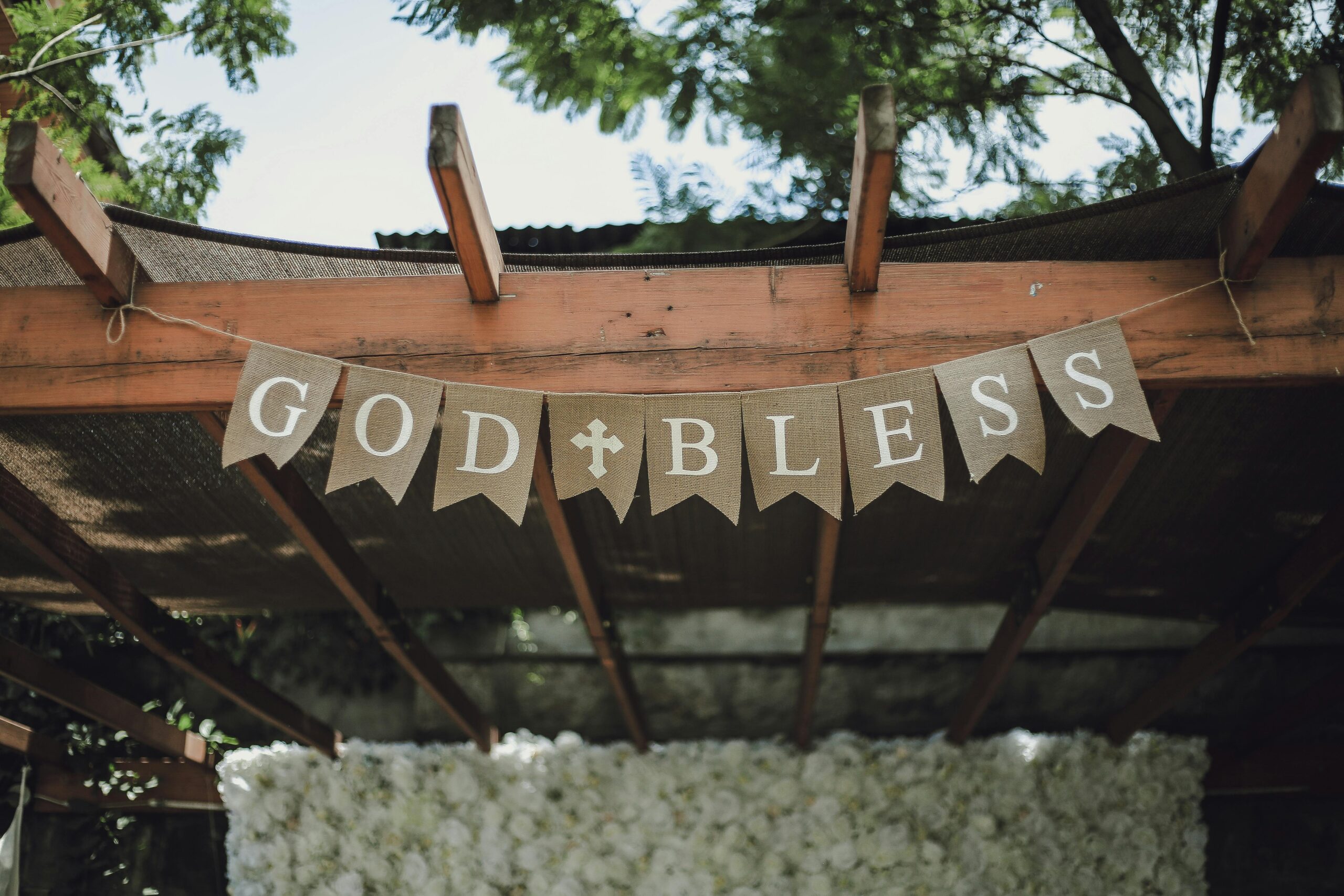 A charming pergola adorned with a 'God Bless' banner, set in a lush, outdoor environment.
