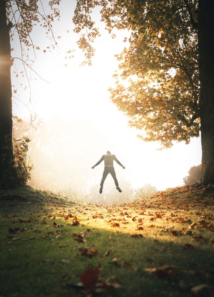 A silhouette of a person leaping midair in a sunlit forest in Srinagar, surrounded by autumn foliage.