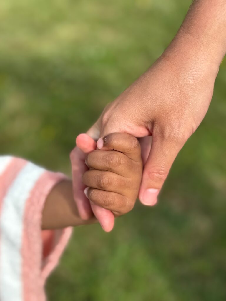 Tender connection between adult and child holding hands outdoors.